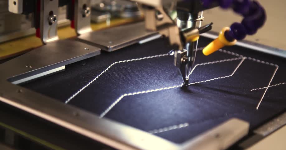 A sewing machine stitches a geometric pattern onto black fabric