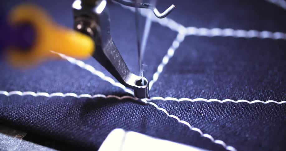 The video shows a sewing machine needle creating a zigzag stitch pattern on a dark blue fabric the camera focuses on the needle as it swiftly moves from side to side pulling the white thread to form a decorative wavy line the surrounding lines of stit
