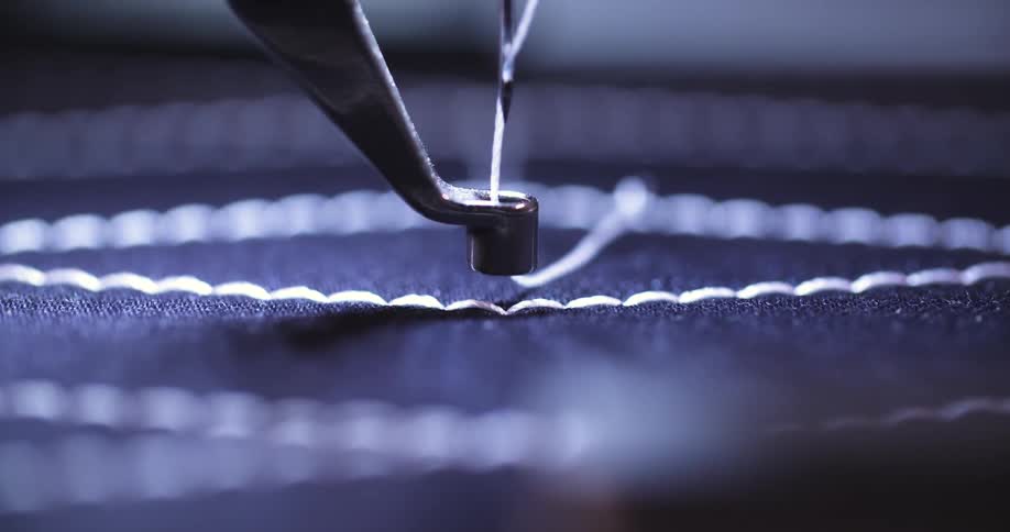 Sewing machine makes a line of stitches on a blue fabric while creating a pattern