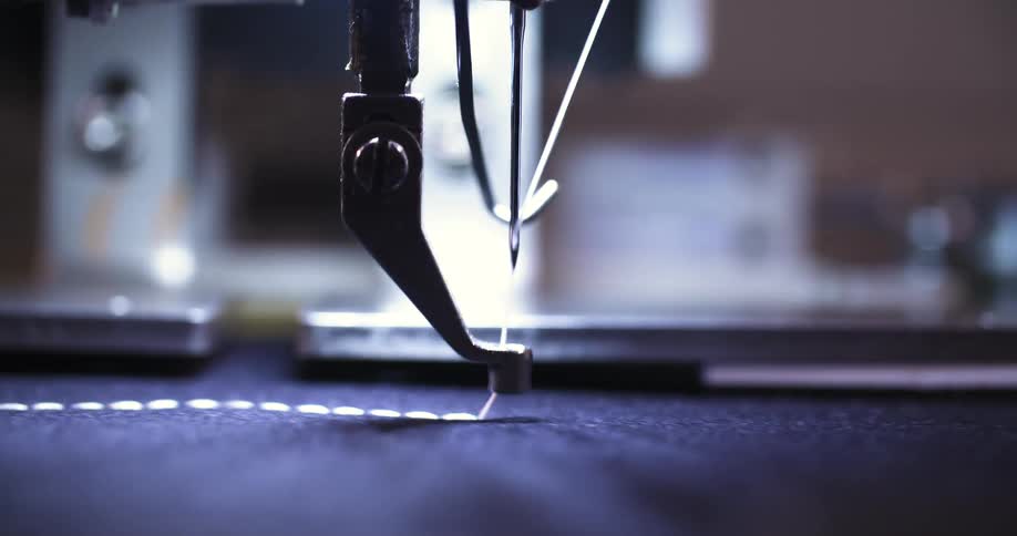 The video is a detailed shot of a sewing machine in action a needle rapidly moves up and down pulling a white thread through a dark fabric creating a line of evenly spaced stitches the focus is sharp on the needle highlighting the precision of the au