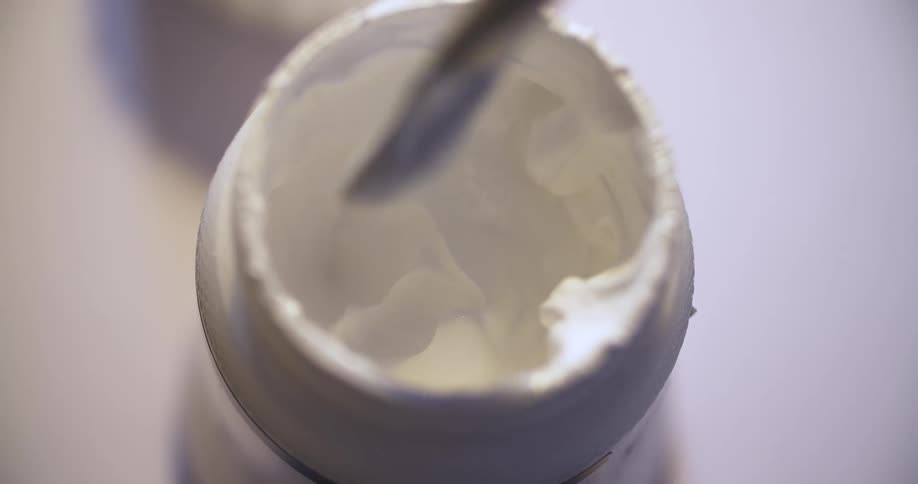 Person dipping a paintbrush into a container of white paint