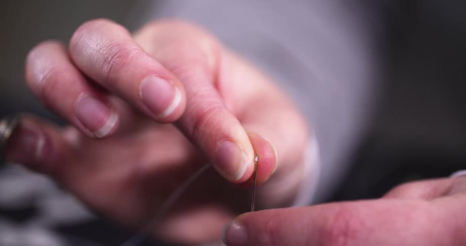 A closeup of hands threading a needle