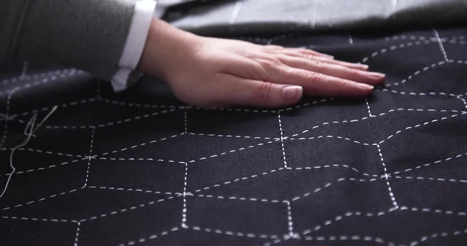 A hand smooths dark fabric patterned with white stitched geometric lines with scissors resting nearby