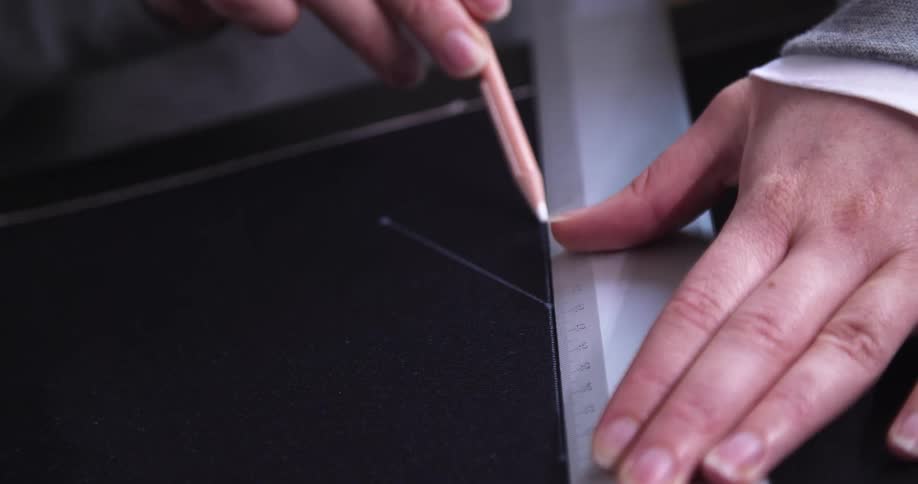 A tailor uses a pencil and metal ruler to measure sizes on fabric