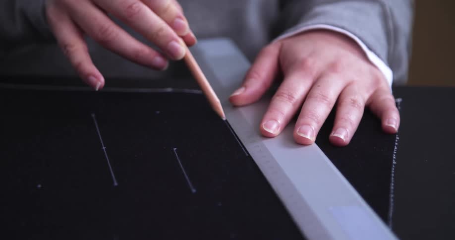 Person using a ruler and pencil to mark lines on dark fabric