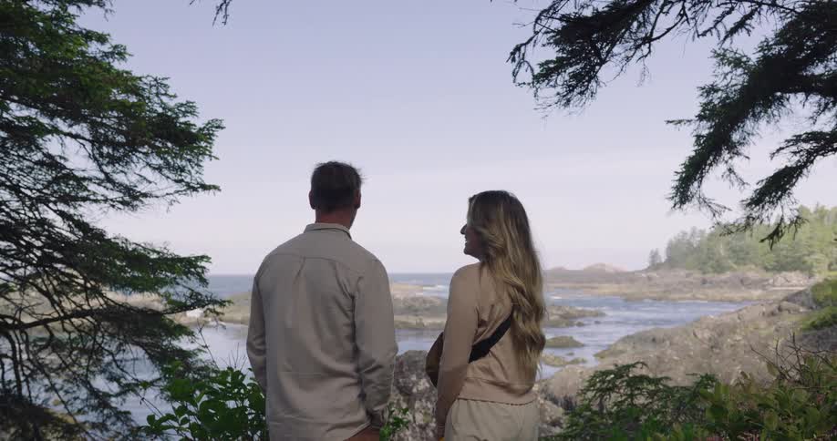 Two people stand on a cliffside overlooking the ocean turning to face each other and speaking