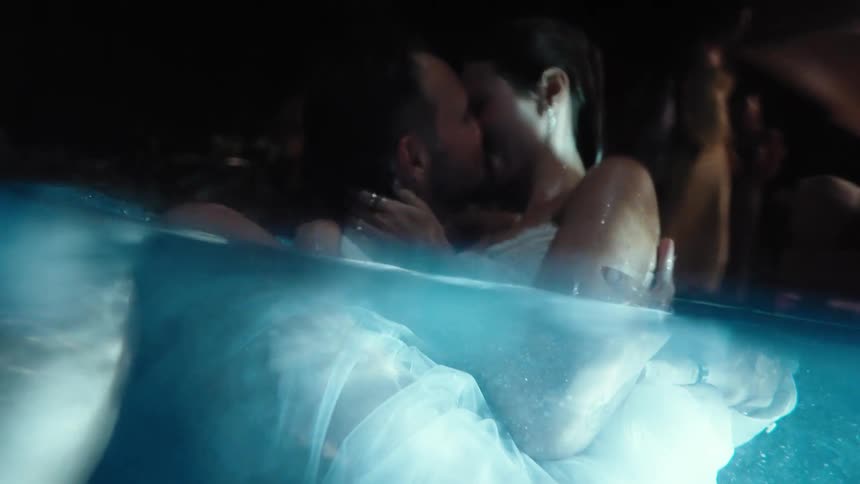 Close up of a young couple kissing while holding each other in a pool at an event at night