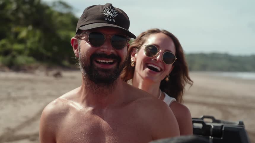 Smiling couple wearing sunglasses enjoys a motorcycle ride on the beach
