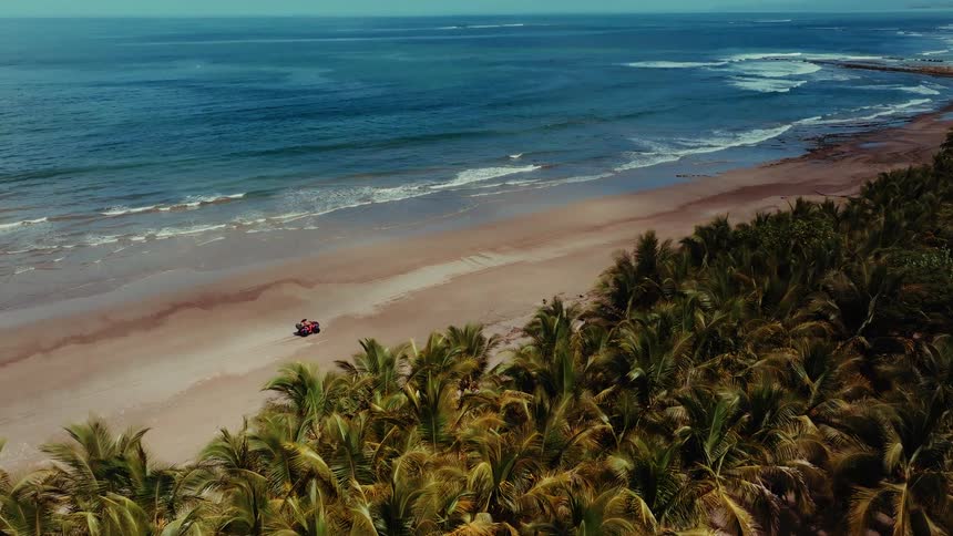 An atv drives along a sandy beach shoreline on a sunny day