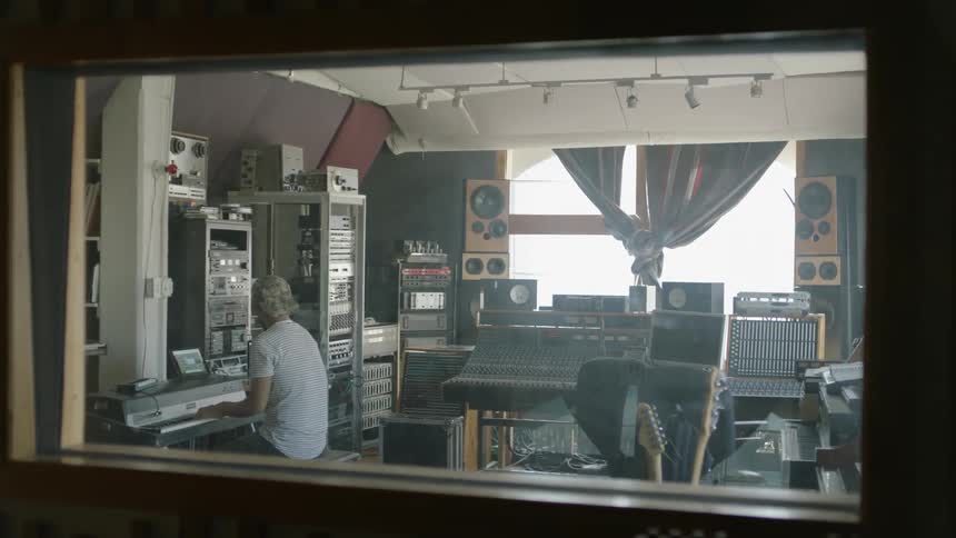 A man is sitting in a music studio playing a keyboard