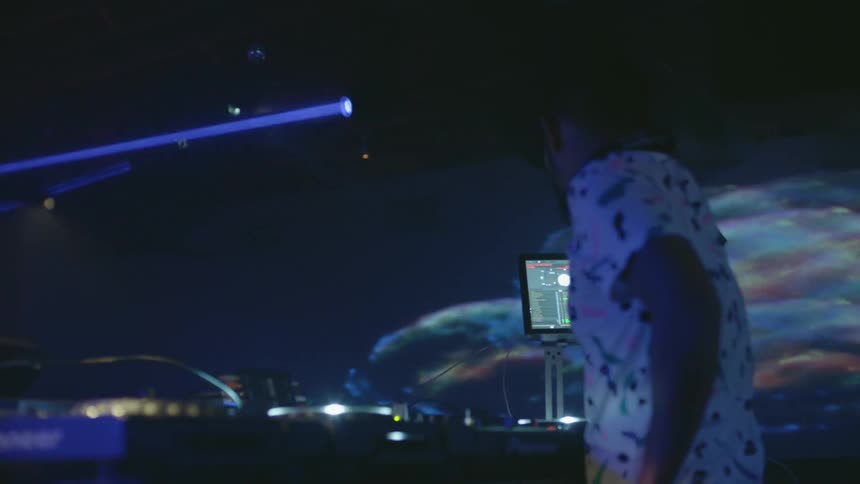 A dj stands behind sound equipment at a nightclub