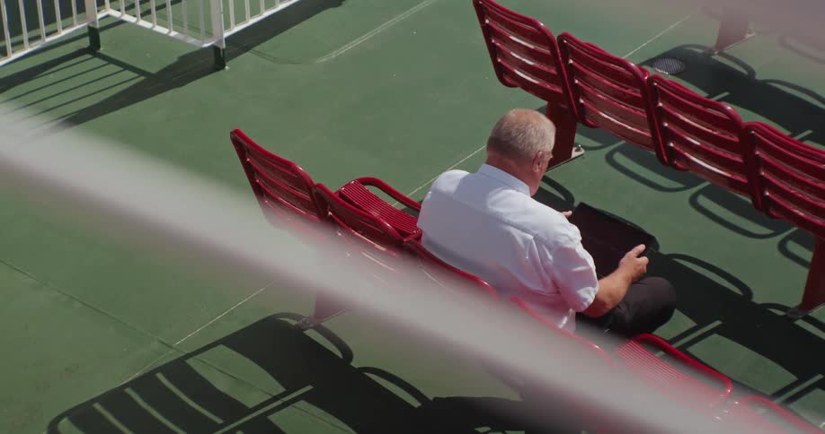 Man sitting on a red stadium chair looks at a screen in his lap