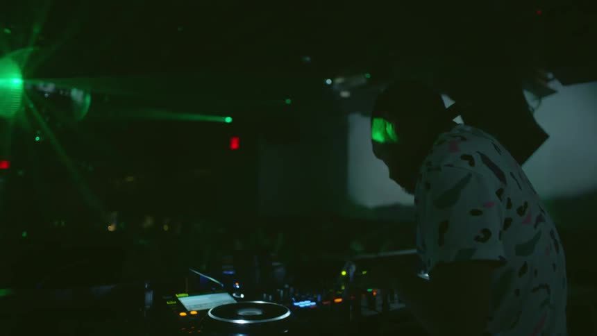 A dj plays music as lights shine on a disco ball