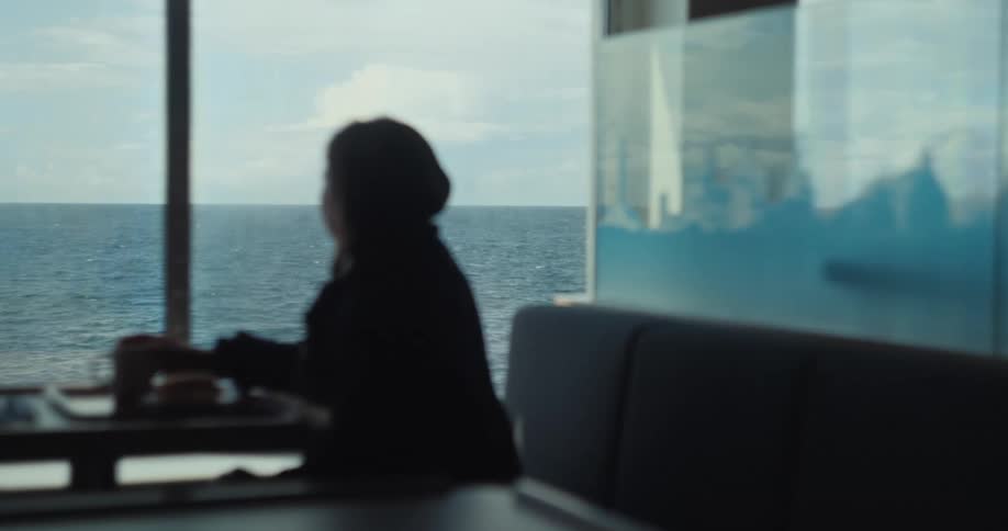 Person sitting by a window looking at the sea while having coffee