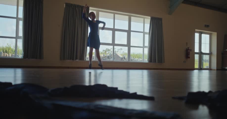 A female teenager practices dance moves in a large room during daytime