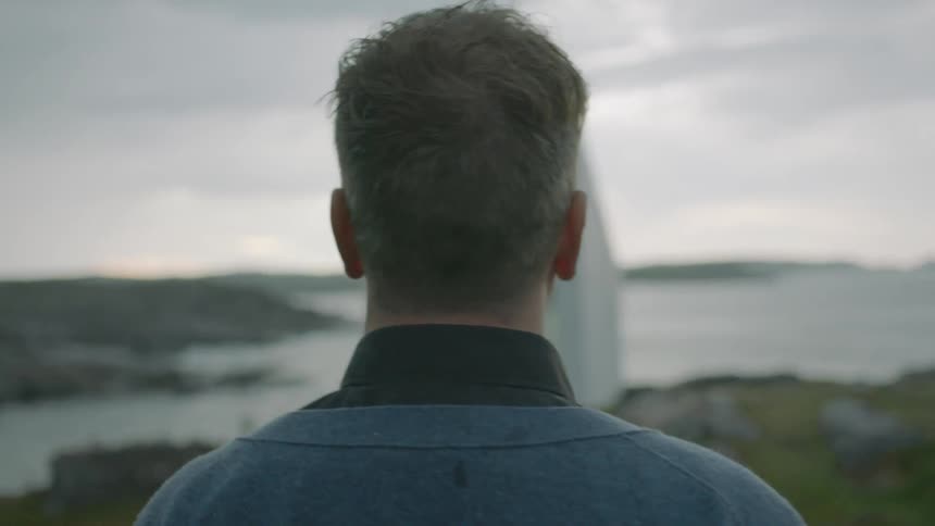A man looks at a small house by the water