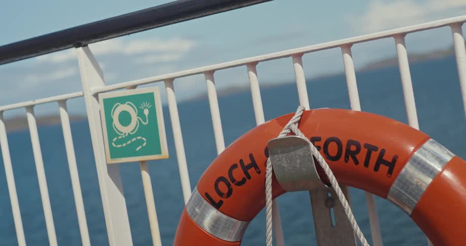A life preserver hangs from a railing on a boat with water and sky in the background