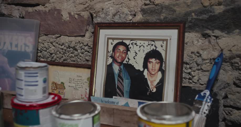 Photograph in a picture frame on a bookshelf next to a brick wall