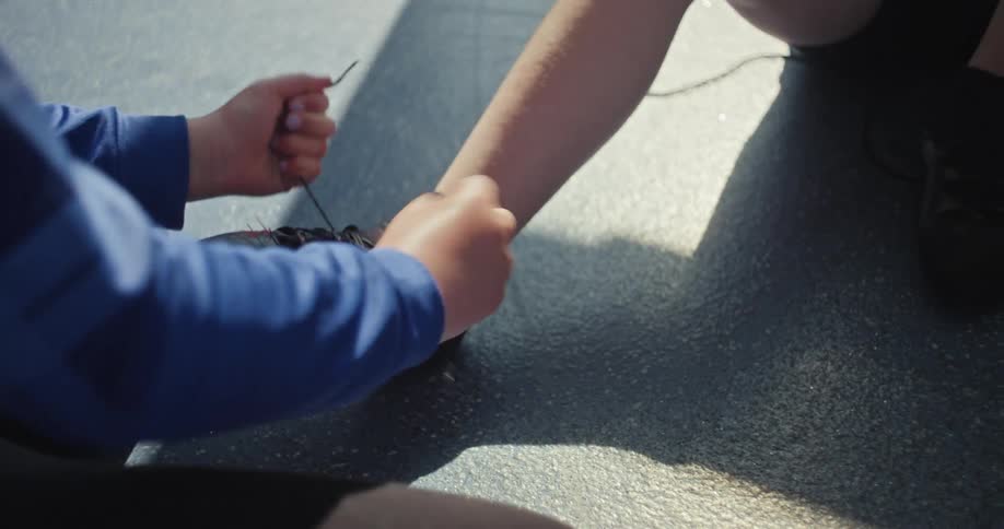 A persons hands are shown tying the laces of a shoe on the ground