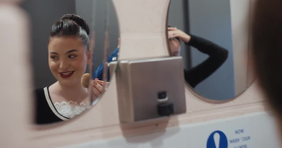 Two women putting on makeup in front of the mirror