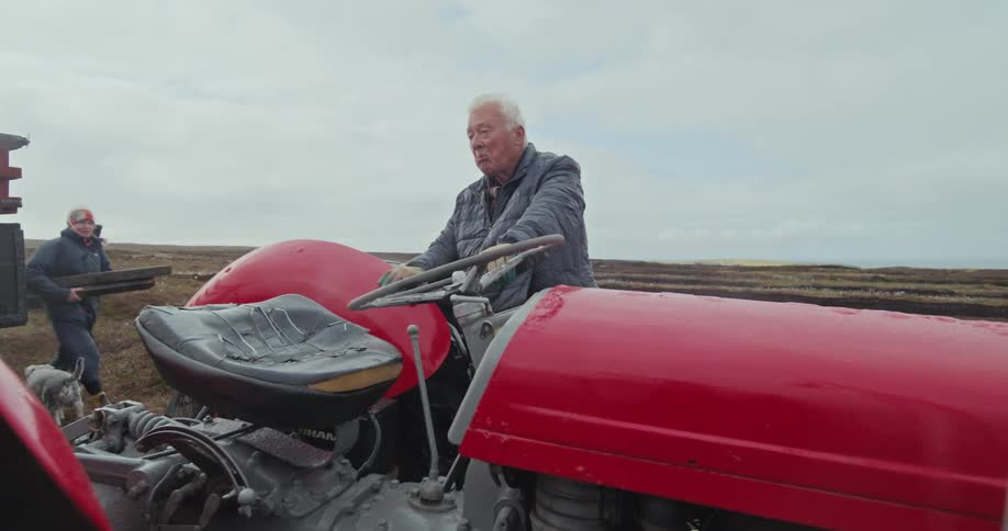 Elderly man standing next to a red tractor on a farm