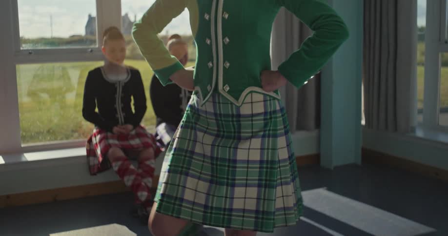 A person dances their kilt swinging while two other people watch in the background