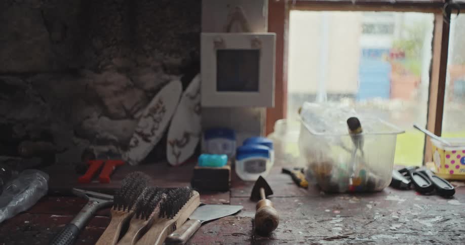 A wide angle view shows a messy workbench with a variety of brushes tools and plastic containers in front of a window