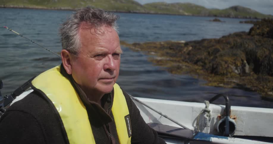 Man wearing a yellow life jacket rides a boat near the rocks