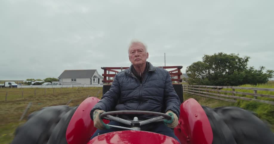 Elderly man driving a tractor through a farm