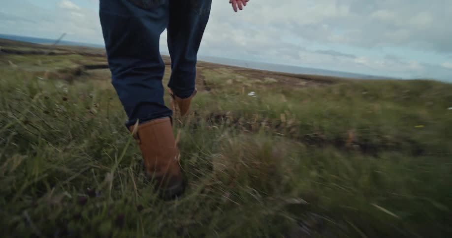 A person wearing boots and jeans walking through bushes to get to a grass plain