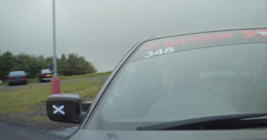 A car on a test track driving away from its parking near a cargo container