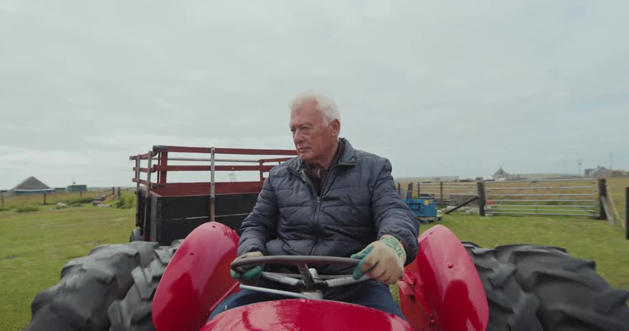 Man driving a red tractor in a rural area with a barn in the background