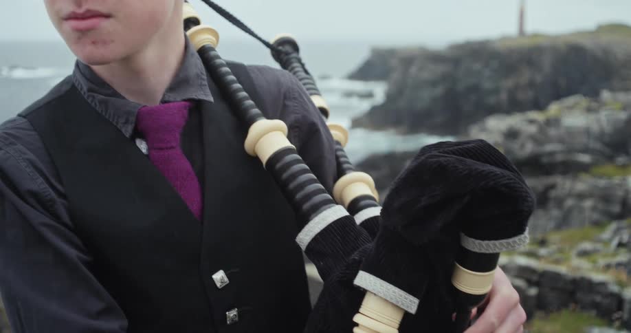 The teenager is holding his bagpipes by the shore