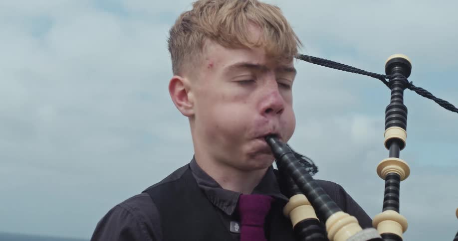 Young man playing bagpipes outdoors under a cloudy sky