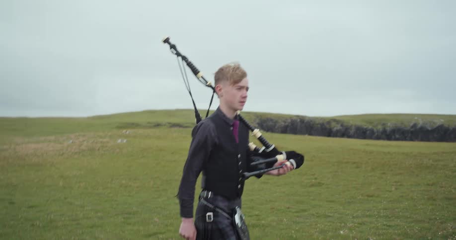 Young man in scottish kilt walks with bagpipes in an open field