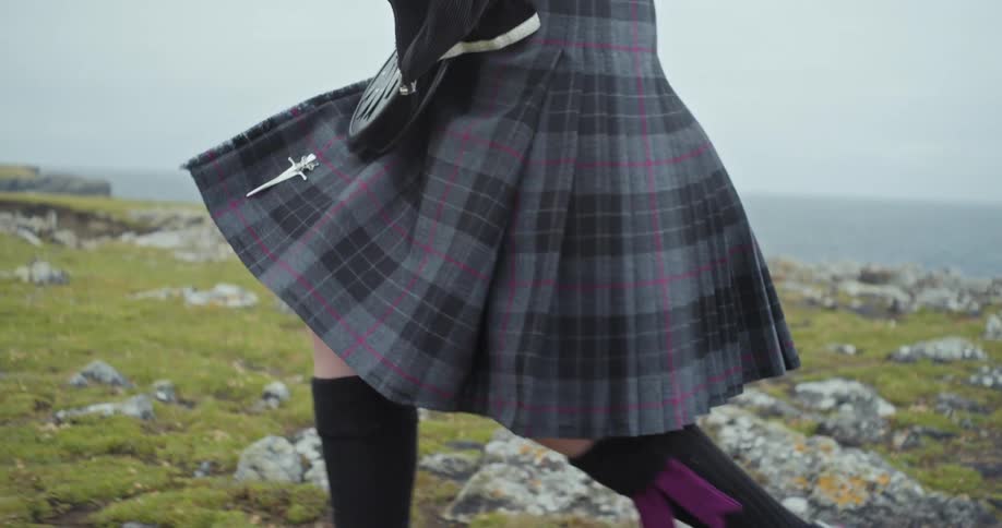 The person walks by the cliff wearing a kilt