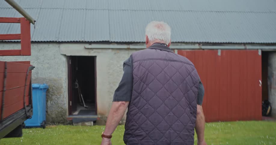 A person wearing blue jeans and work boots loads buckets of peat into a barn