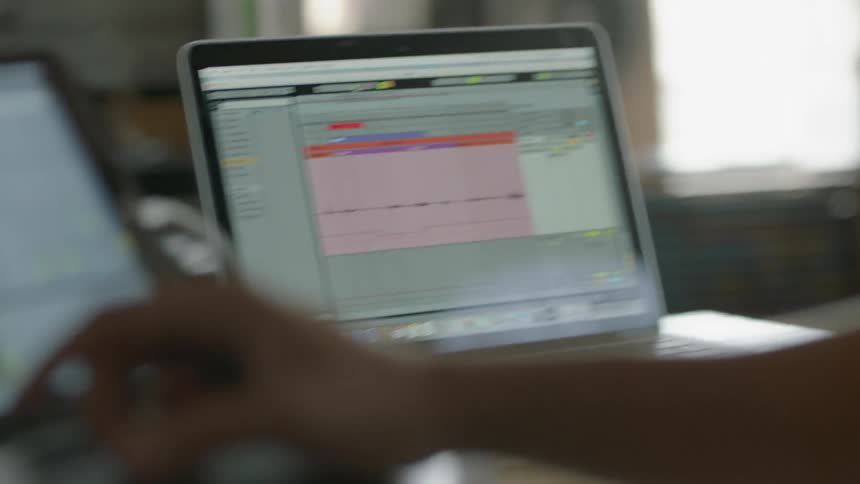 A person working on a laptop makes an adjustment on another monitor