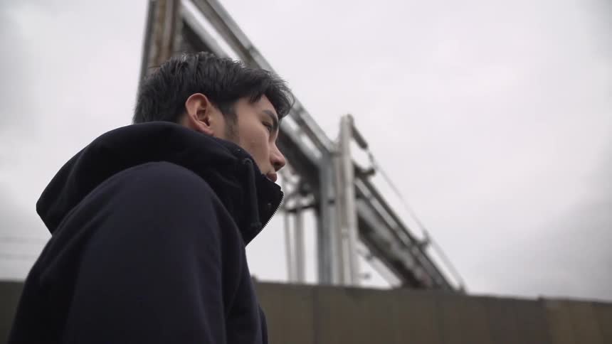 A young man walking pasta a building in an industrial area under a cloudy sky