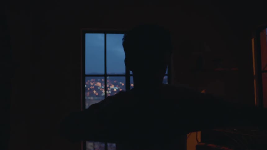 A man puts on a shirt in a dark room