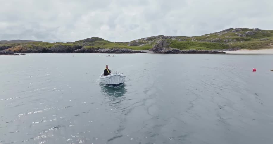 Man in a small boat sailing in calm waters near a rocky island