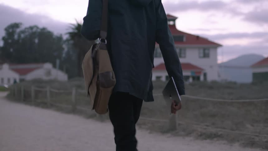 A man walks down a dirt road carrying a tablet
