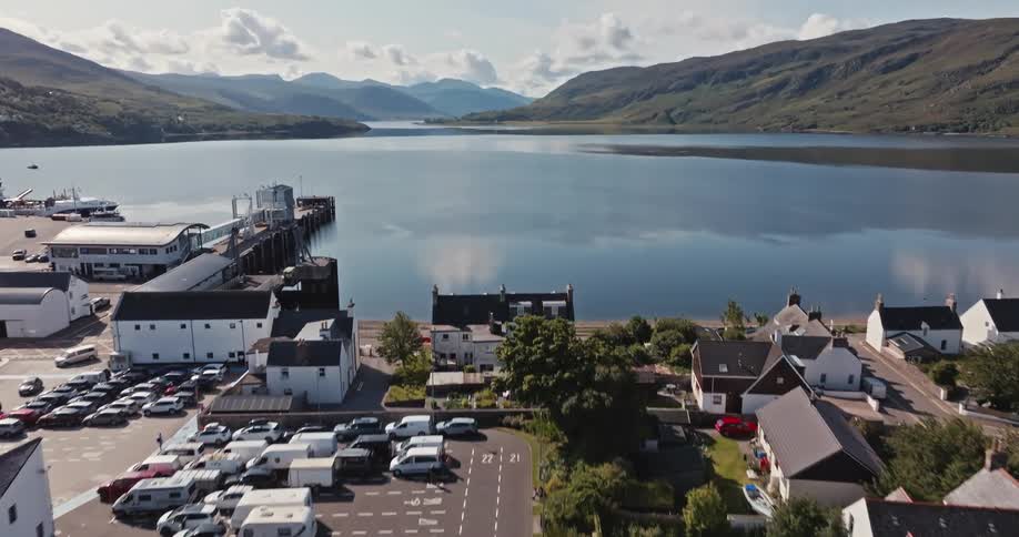 An aerial shot begins above a suburban neighborhood and then rises to reveal a large bay with a pier and a town nestled between green mountains