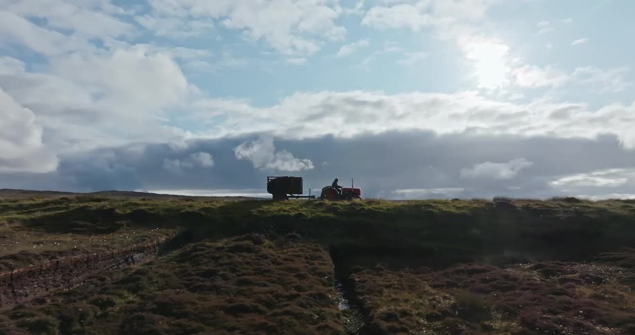 A tractor with a trailer driving across a plowed field