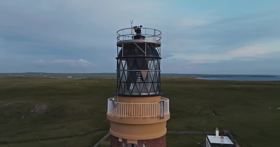 In the first clip a figure in a white spacesuit walks through a narrow crimsonlit hallway the second clip is an aerial shot that shows a lighthouse perched on a grassy coastline with the surrounding ocean and hills visible in the background