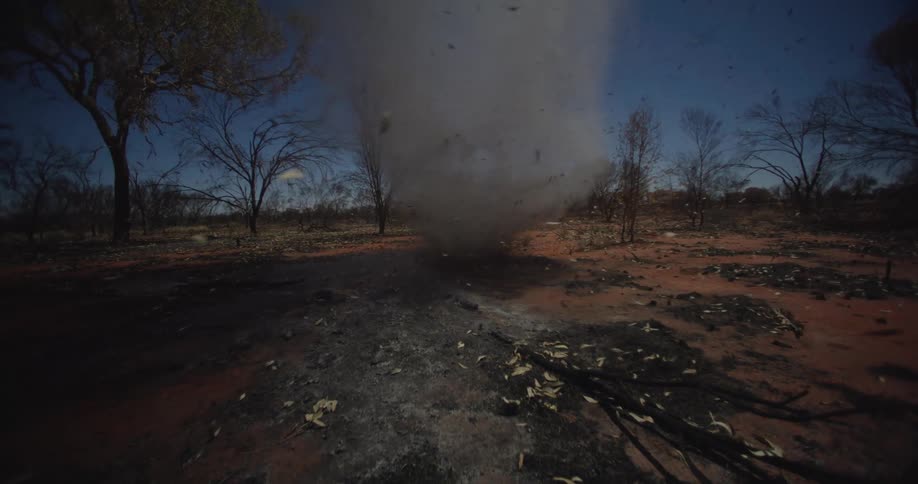 A swirling column of dust and debris rotates on the dry ground in a barren landscape