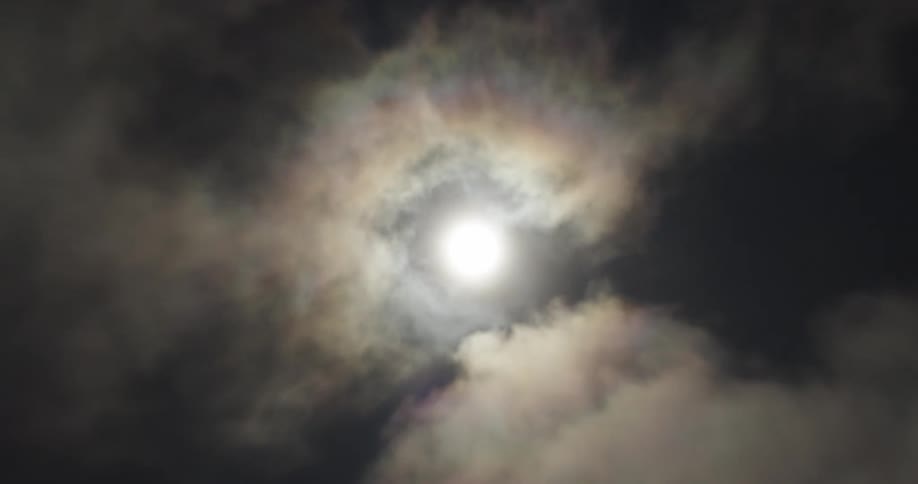 The video shows a closeup static shot of a bright moon obscured by wispy clouds the clouds drift across the face of the moon creating a dynamic and ethereal effect