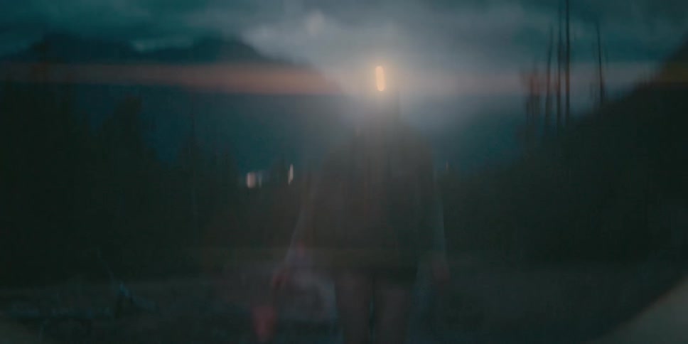 A woman wearing a headlamp runs in the dark at the base of mountains under a cloudy night sky