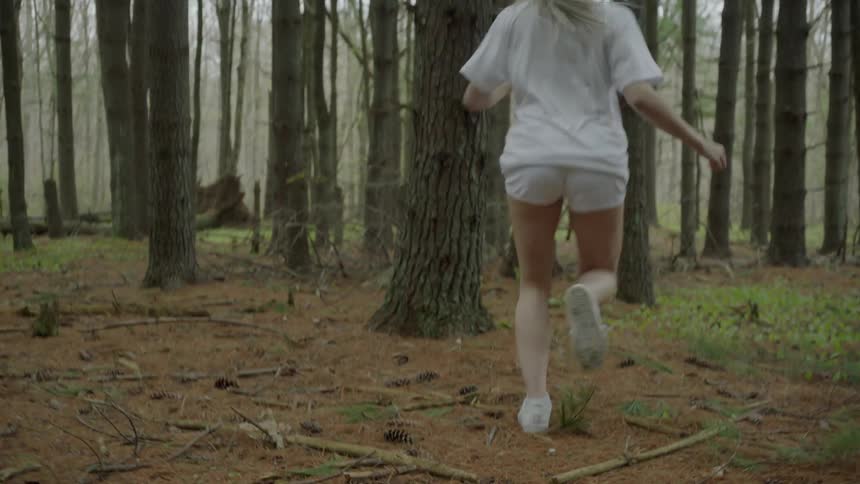 A woman runs in the forest dodging trees