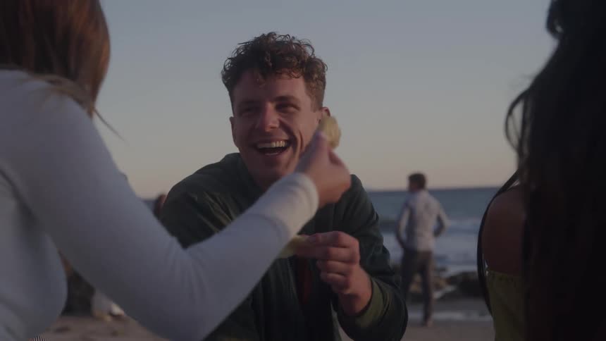 Friends laugh and eat on the beach